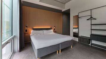 Een moderne hotelkamer met een groot bed, een kledingkast met planken, een nachtkastje en een raam met gordijnen.