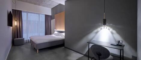 A modern hotel room with a bed, a desk with a chair, a mounted TV, and a large window with curtains.