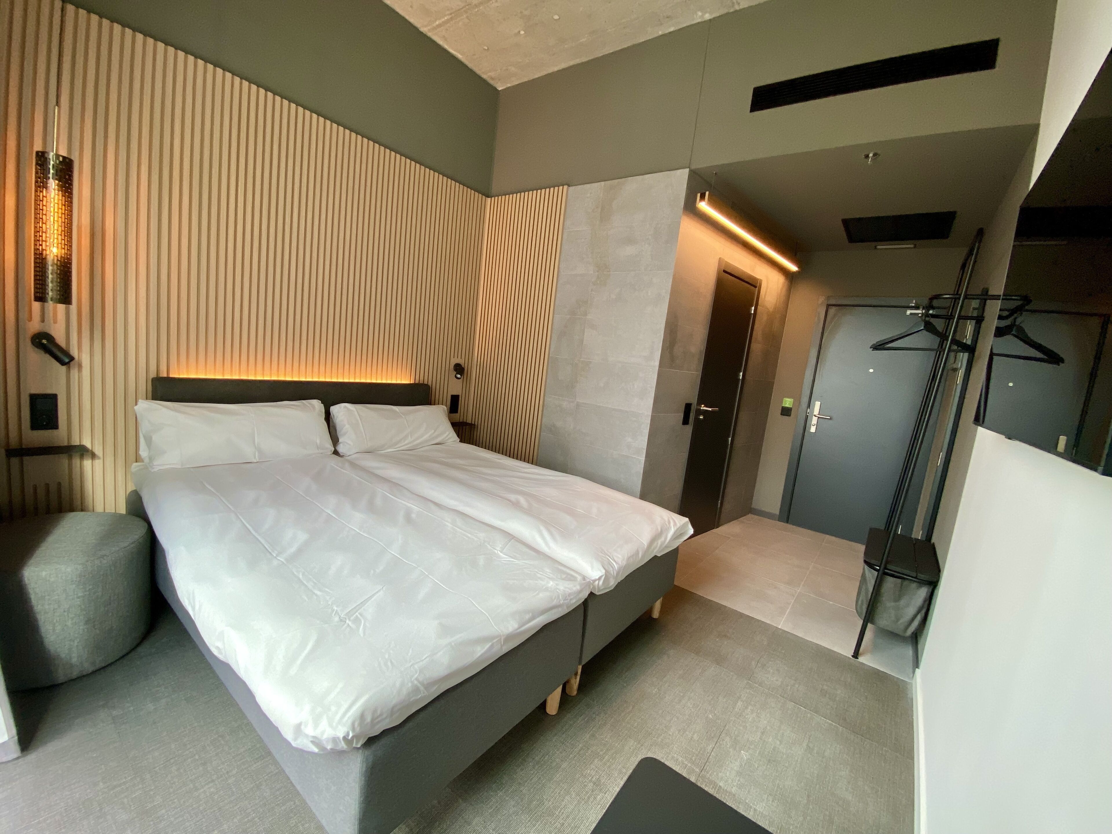 A modern bedroom with a large bed, a bedside table, a wall-mounted light, and a door leading to a closet.