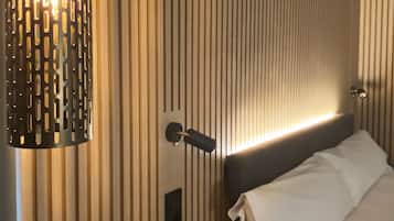 Una habitación de hotel con papel tapiz a rayas verticales, una cama con ropa de cama blanca, una mesita de noche negra y una lámpara de pared.