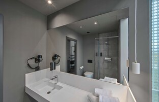 Ein modernes Badezimmer mit großem Spiegel, weißem Waschbecken und einer Duschkabine aus Glas.