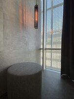 Una camera moderna con un pouf rotondo, una lampada a sospensione e un'ampia finestra con vista all'esterno.
