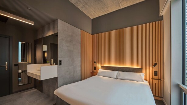 A modern hotel room with a large bed, a built-in vanity with a mirror, and a wooden panel wall. - Zleep Hotel Madrid Airport (Madrid)