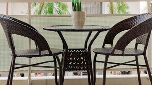 Un balcón con sillas de mimbre y una mesa, rodeado de exuberante vegetación.