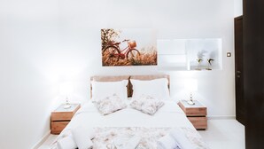 Una cama bien hecha con ropa de cama floral, dos mesitas de noche con lámparas y una obra de arte colgada en la pared que representa una bicicleta.