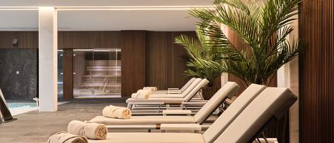 A modern indoor pool area with lounge chairs, towels, and a large potted plant.
