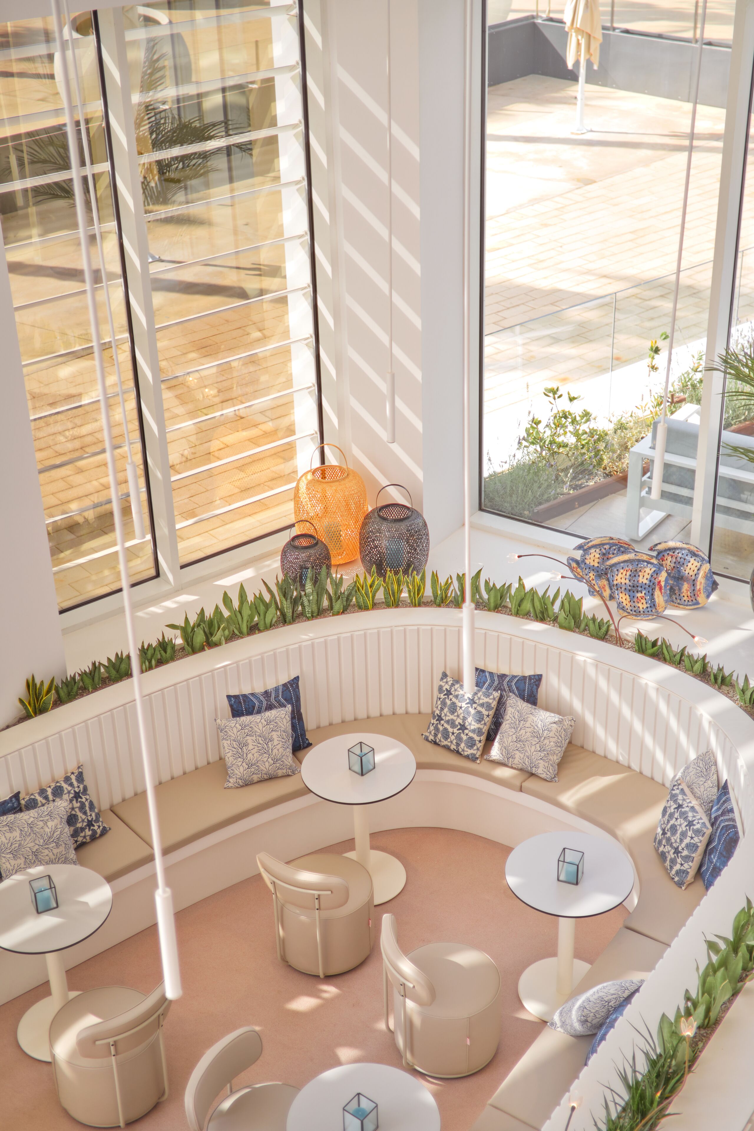 A modern lounge area with a curved seating arrangement, round tables, and a view of the outdoor patio through large windows.