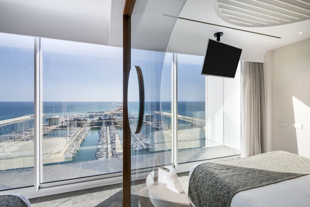 A modern hotel room with a large window offering a view of a marina and boats.