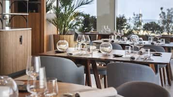 En restaurang med bord som är dukade för middag, och med utsikt över havet.