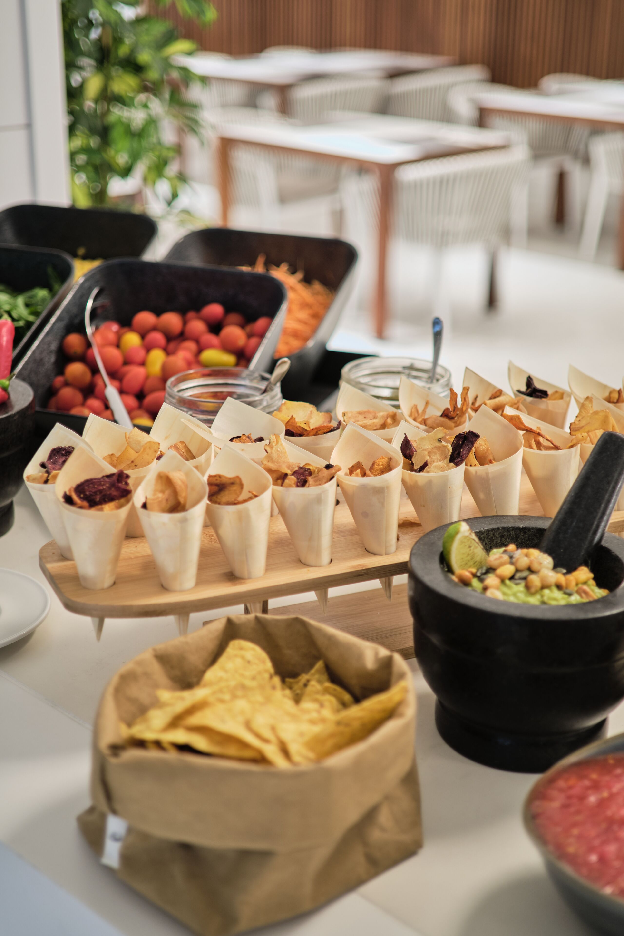 A buffet table with various food items including chips, dips, and a bowl of guacamole.