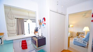 A compact room with a kitchenette, a mirror, a hanging light fixture, and a view into a living area with a chair and a lamp. - Bridgepoint II 5D-Bayfront 94th St, Free WiFi, Pool, W/D, AC (Ocean City)