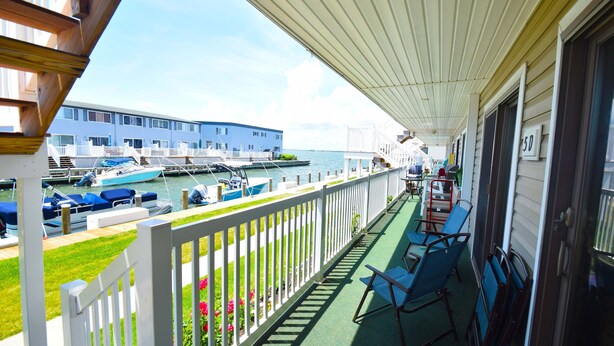 A covered balcony with a view of the marina, outdoor seating, and a building in the background. - Bridgepoint II 5D-Bayfront 94th St, Free WiFi, Pool, W/D, AC (Ocean City)
