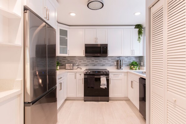Features a kitchen with stainless steel appliances, white cabinetry, and a tiled backsplash.