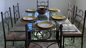 A dining area with a glass table, metal chairs, a chandelier, and a view through a window.