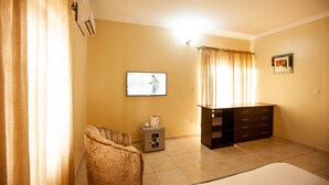 A hotel room with a bed, a small cabinet, a chair, a television, and a window with curtains.