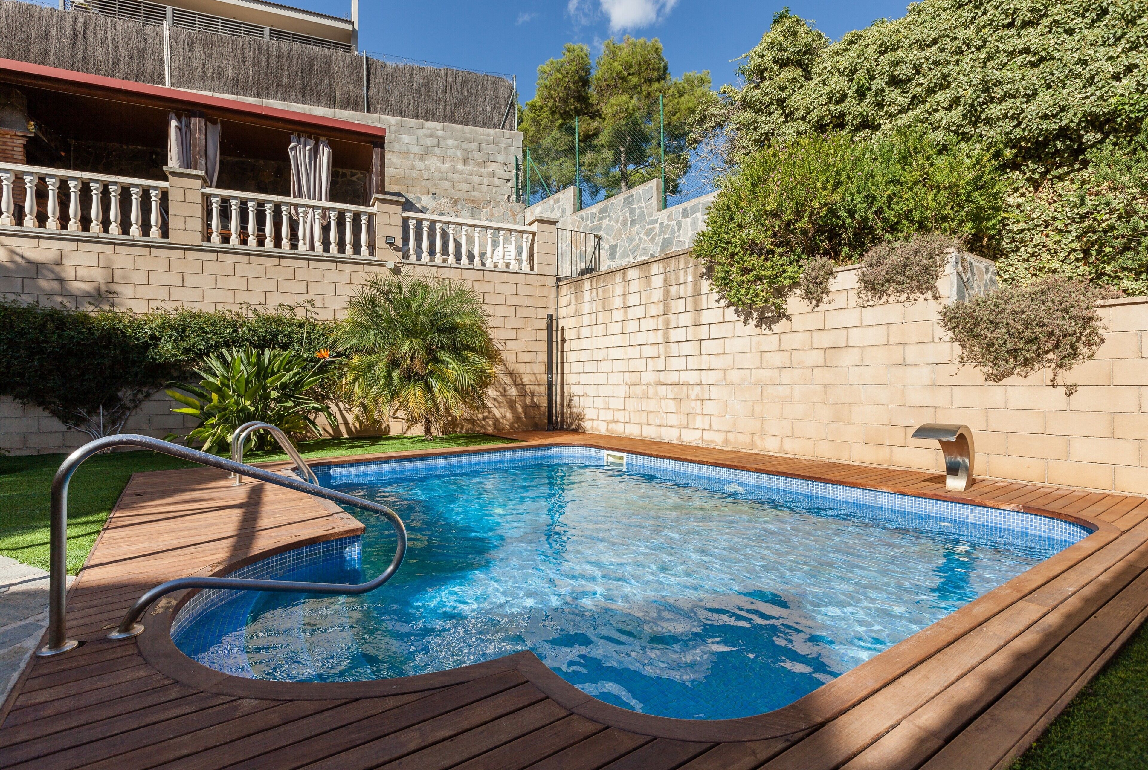 Une piscine avec une terrasse en bois, un mur en pierre et un balcon doté d’une balustrade.