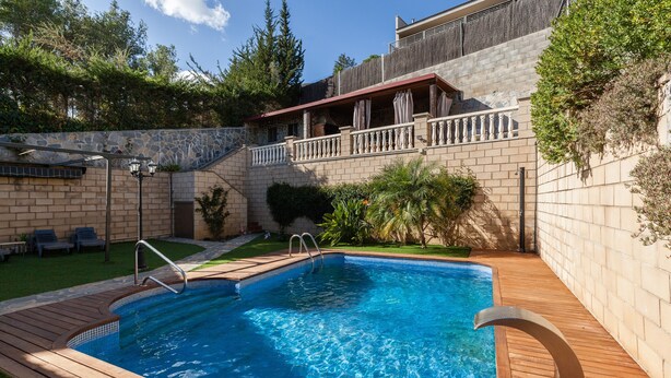 Ein Schwimmbecken mit Holzterrasse, einer Steinmauer und einem Balkon mit Geländer.