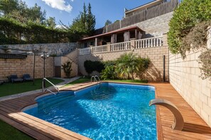 Piscina com deck de madeira, parede de pedra e varanda com guarda-corpo.