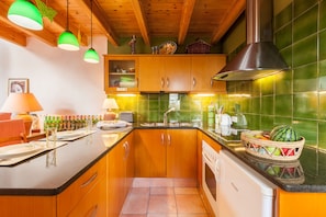 Een keuken met houten kastjes, een zwarte afzuigkap en een betegelde spatwand.