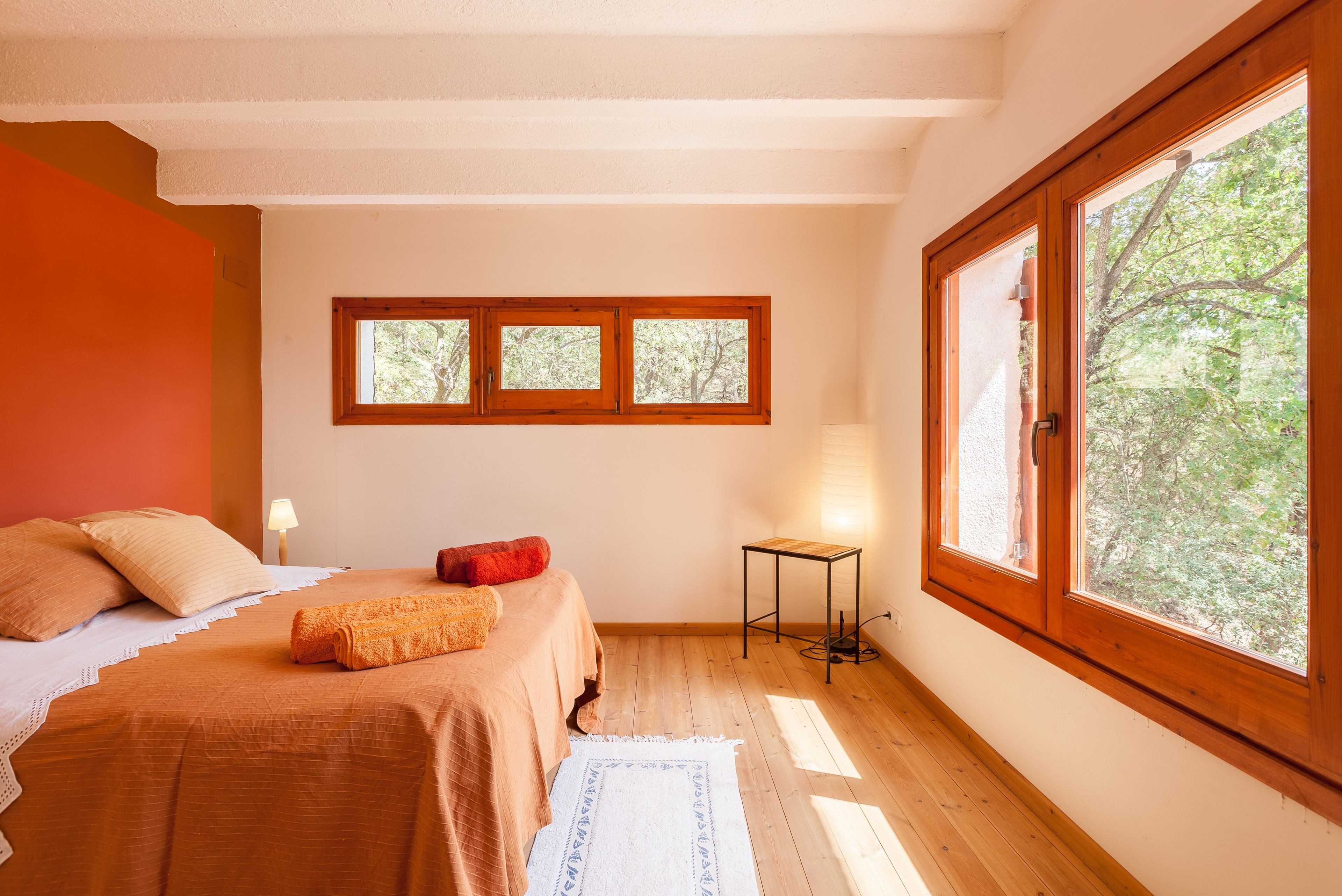 A bedroom with a bed, a nightstand, a lamp, and a window with a view of trees.