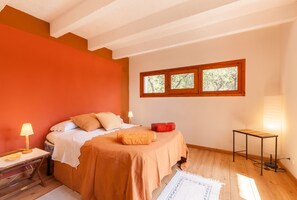 Ein Schlafzimmer mit einem Bett, einem Nachttisch, einer Lampe, einem Fenster und einem kleinen Tisch.