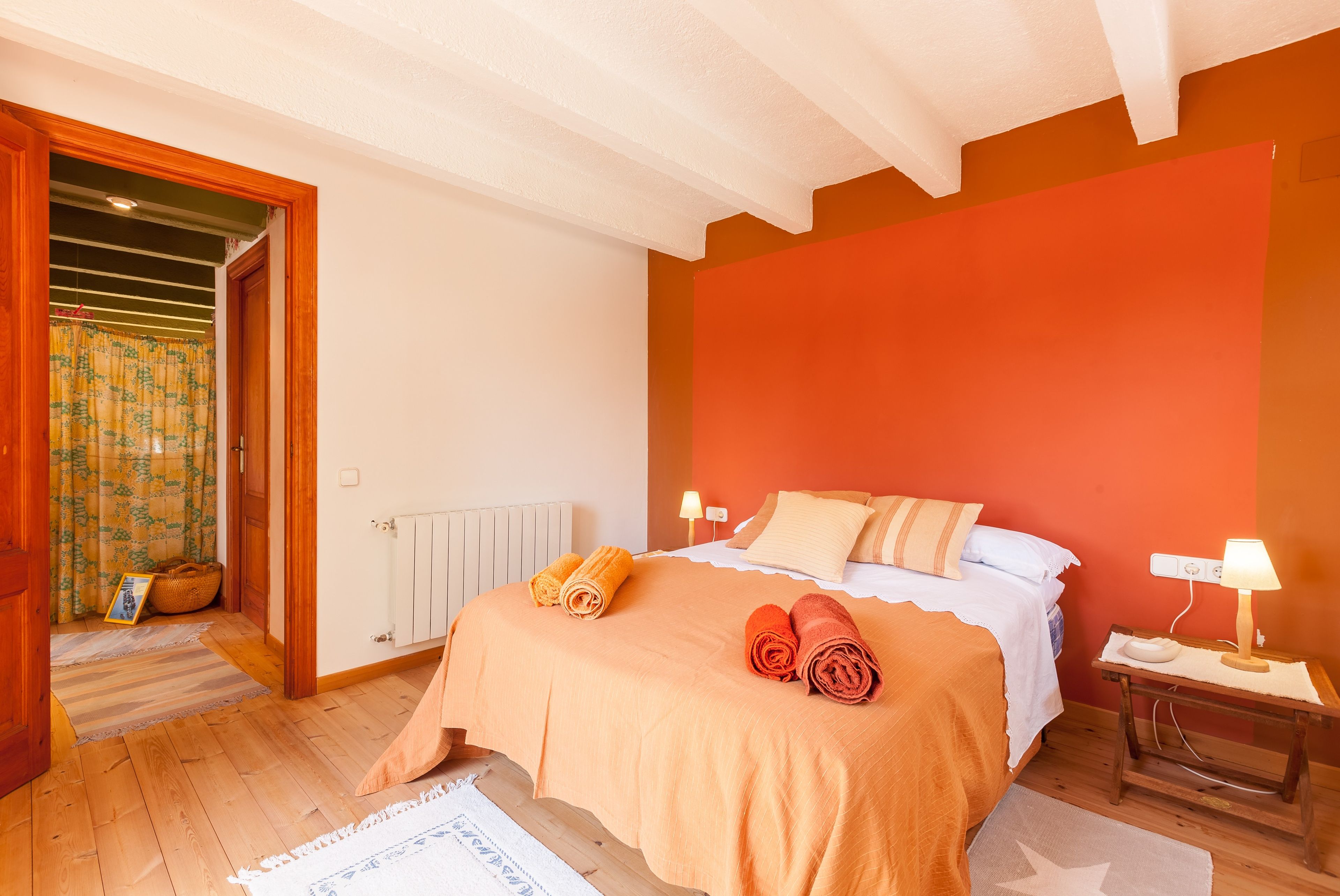 Une chambre à coucher comprenant un lit, deux lampes de chevet, une table de nuit en bois, un radiateur et une porte donnant sur une autre pièce.