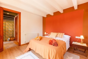 Een slaapkamer met een bed, twee bedlampen, een houten nachtkastje, een radiator en een deur naar een andere kamer.