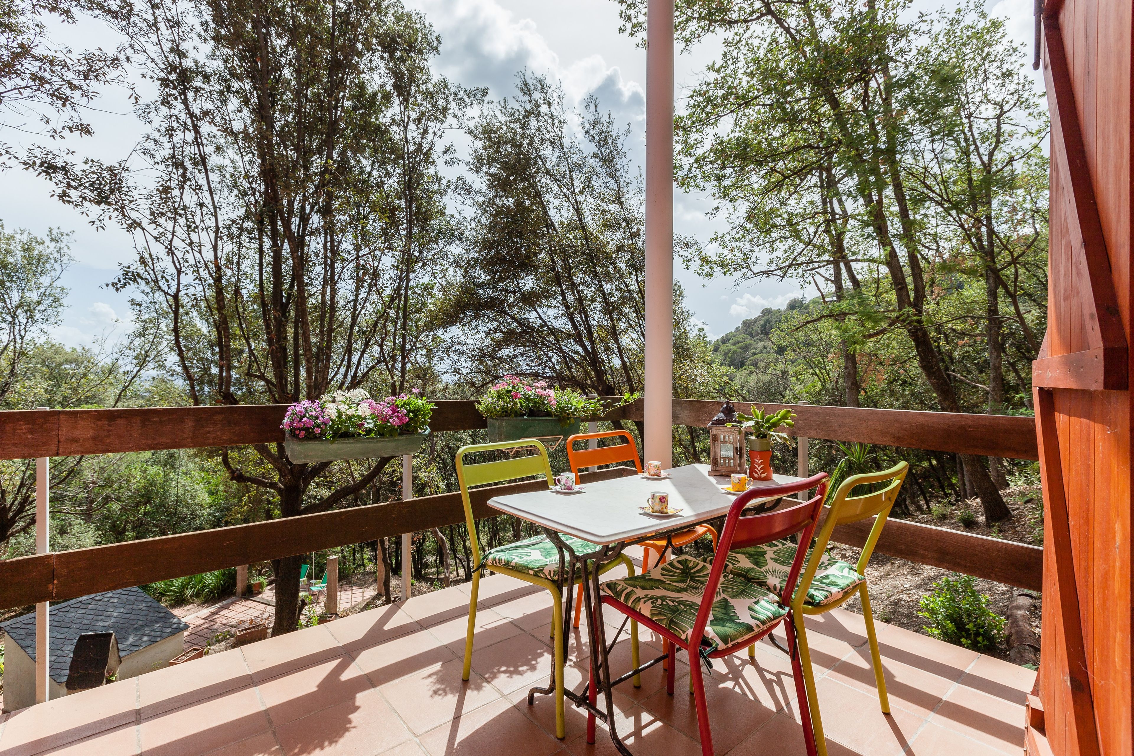 An outdoor patio with a table and chairs, surrounded by trees and a wooden railing.