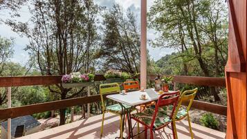 An outdoor patio with a table and chairs, surrounded by trees and a wooden railing.