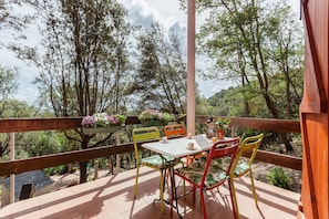 An outdoor patio with a table and chairs, surrounded by trees and a wooden railing.