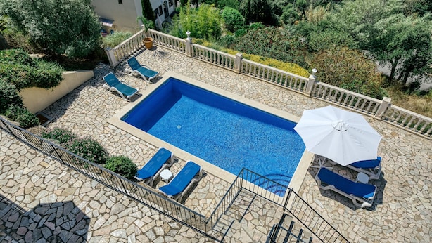 A swimming pool with lounge chairs and an umbrella, surrounded by stone tiles and greenery. - Villa "Castell Mirto" with Private Pool, Terraces & Wi-Fi (Calonge)
