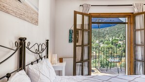 A bedroom with a bed, a bedside table, a lamp, and a view of a balcony with a chair and a table. - Villa "Castell Mirto" with Private Pool, Terraces & Wi-Fi (Calonge)