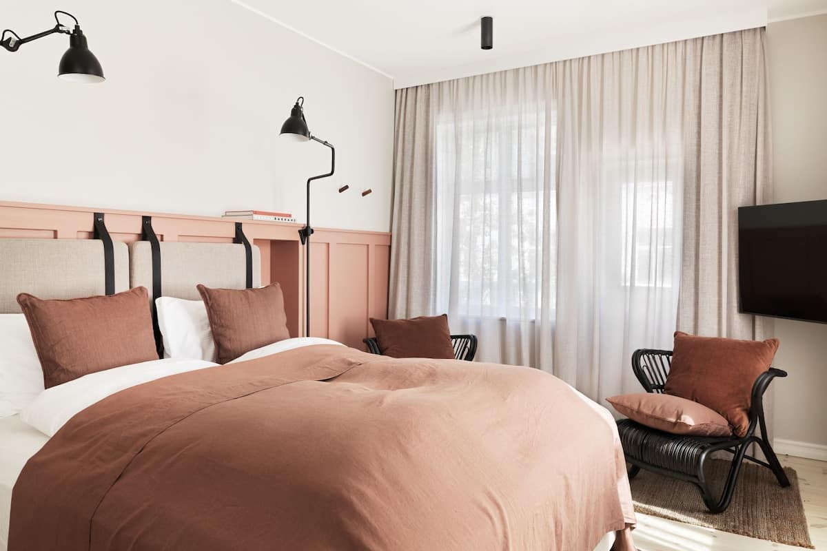 A hotel room with a large bed, two bedside tables, a TV, and a window with curtains.
