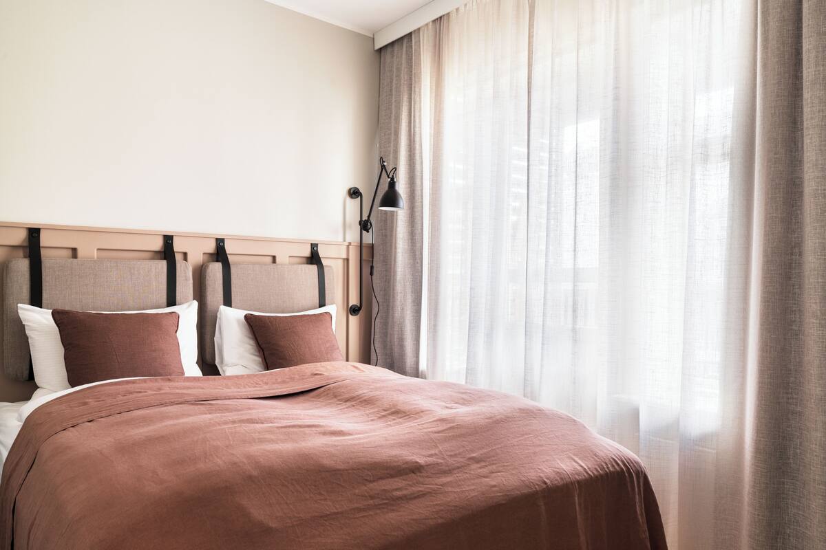 A neatly made bed with a brown bedspread and pillows, a headboard with a light wood finish, and a bedside lamp.