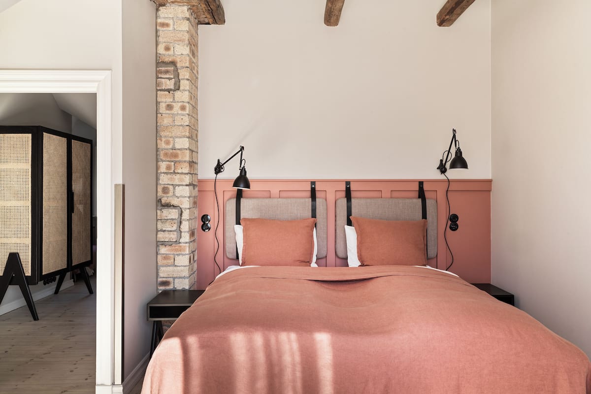 A bedroom with a large bed, wooden headboard, two bedside lamps, and a brick wall.