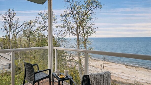 Un balcon avec deux chaises, une petite table sur laquelle se trouve une assiette de nourriture, et une vue sur la plage et l’océan.