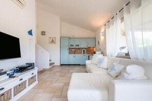 Un salon avec un téléviseur à écran plat, un canapé blanc et une cuisine en arrière-plan.