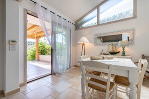 Un coin repas avec une table blanche, des chaises en osier, une lampe et un miroir au mur.