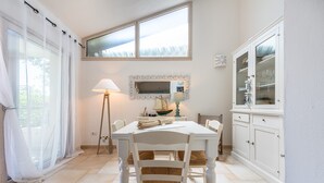 Een eetruimte met een witte tafel, stoelen, een lamp, een spiegel en een kast.
