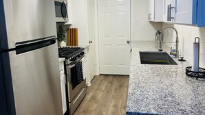 A compact kitchen with white cabinets, a stainless steel refrigerator, a microwave, a stove, and a sink with a modern faucet.