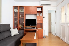 A living room with a grey sofa, wooden entertainment unit, flat-screen TV, and a small wooden table.