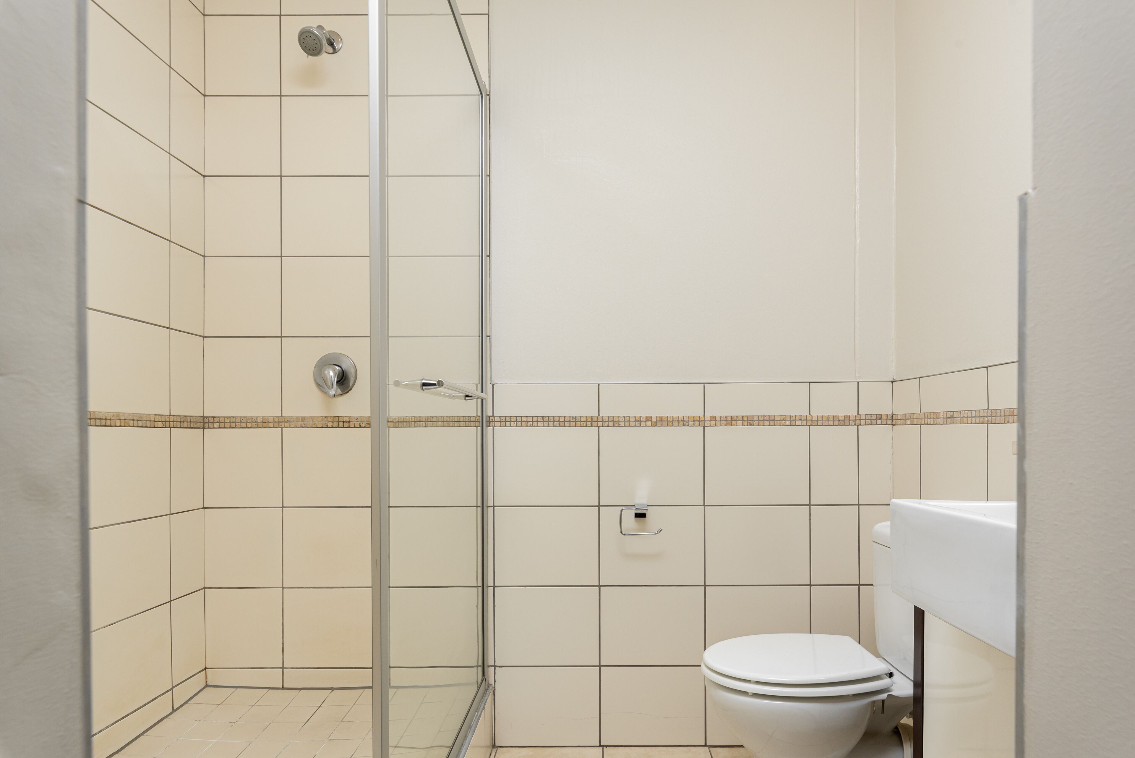 Egy fürdőszoba zuhanyzóval, WC-vel és csempézett padlóval.