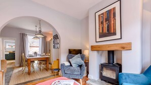 Una sala de estar acogedora con chimenea, un comedor con mesa y sillas, y una cocina visible a través de un arco.