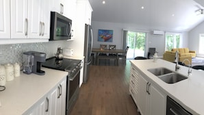 Una cocina moderna con armarios blancos, una isla grande con un lavamanos y un comedor con un sofá y sillas amarillos.