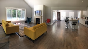 Un salón amplio con chimenea, sofás amarillos y un ventanal grande con vistas a un bosque.