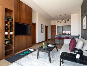 A modern living room with a TV, exercise equipment, and a kitchen area with bar stools. - Swissotel Living Jeddah (Jeddah)