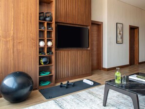 Ein Raum mit einer Wandverkleidung aus Holz, die Trainingsgeräte, einen großen schwarzen Gymnastikball, eine schwarze Trainingsmatte und einen mit Marmorplatten belegten Tisch mit einem Buch und einer Flasche beherbergt.