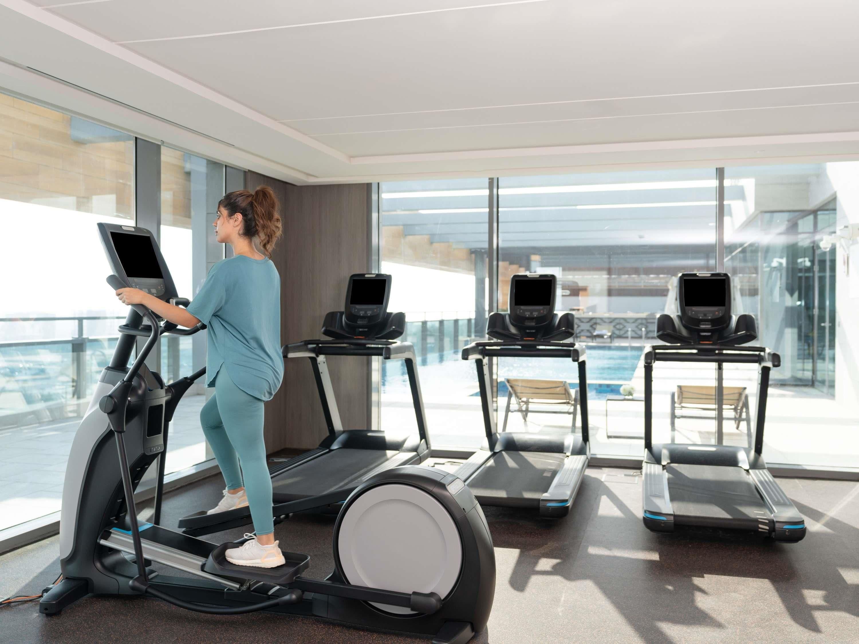 A modern gym with treadmills and a large window overlooking a pool.