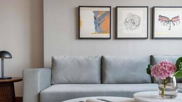 Una sala de estar moderna con un sofá gris, una mesa redonda de centro con un libro y una taza roja, un jarrón con flores rosas, y tres cuadros en la pared.