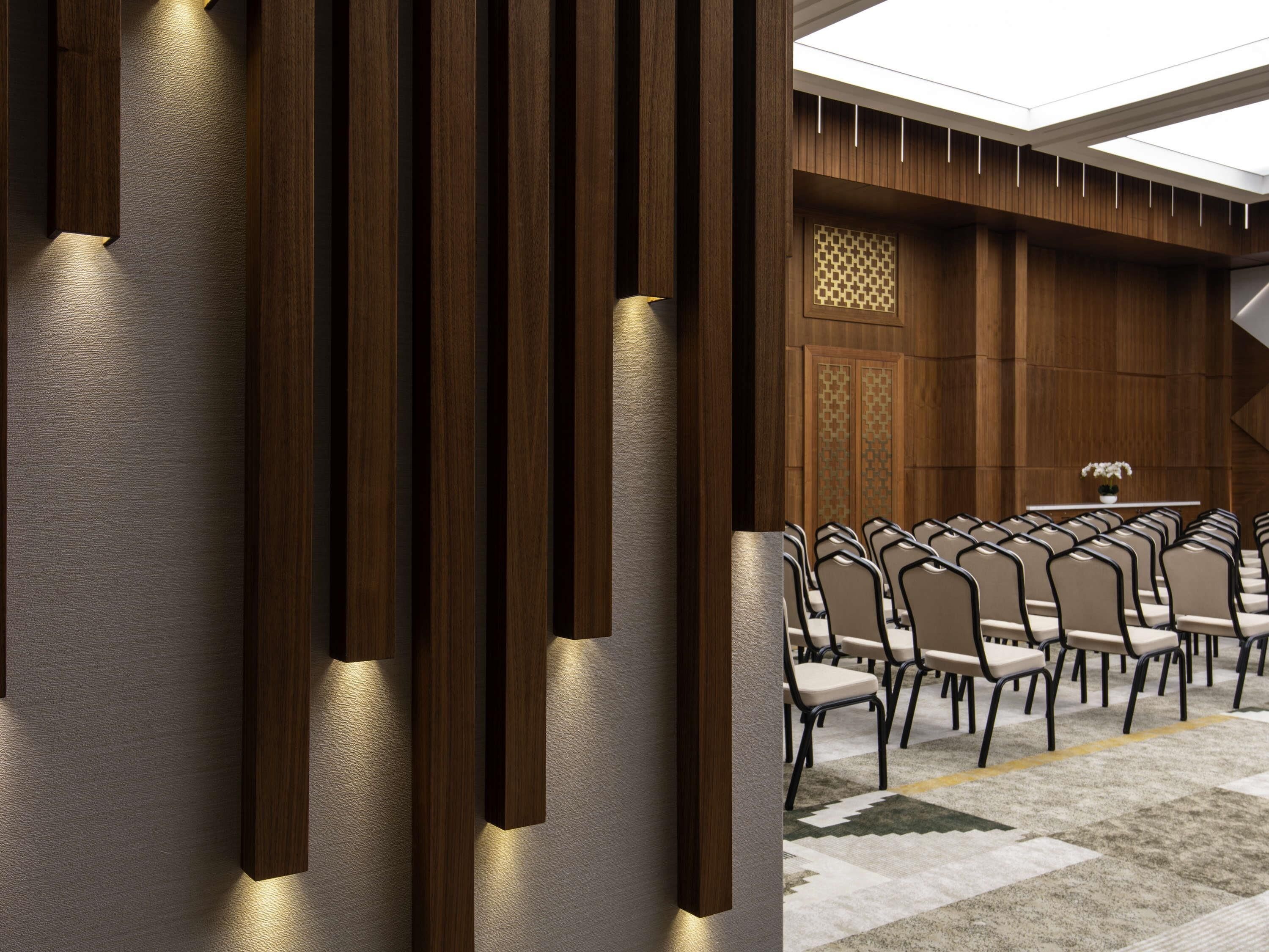 A conference room with a long table and multiple chairs, wooden paneling, and a patterned wall design.